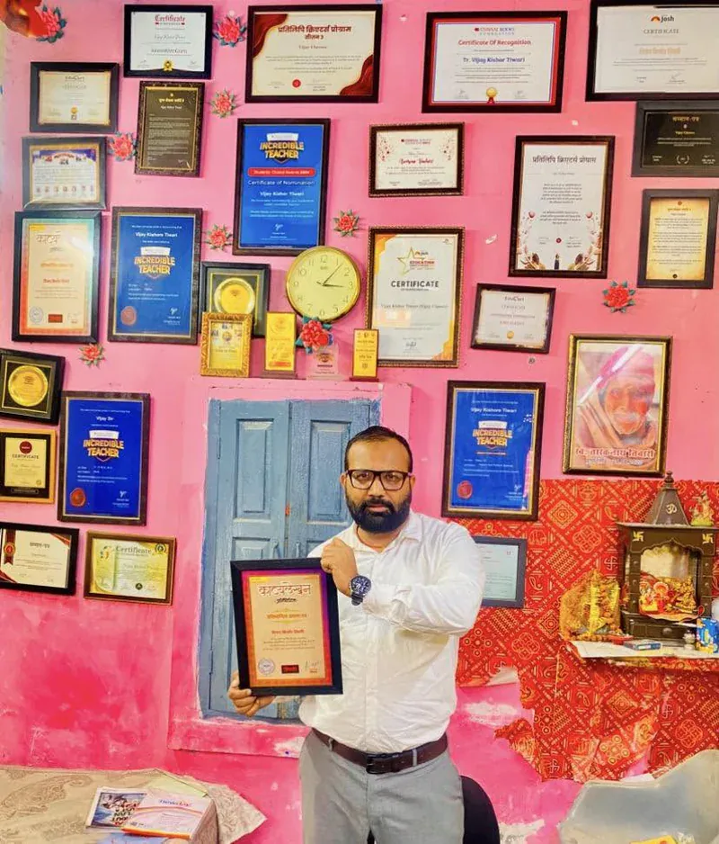 Vijay Kishor Tiwari holding his Kavyalekhan competition certificate in front of the wall of certificates at Vijay Classes