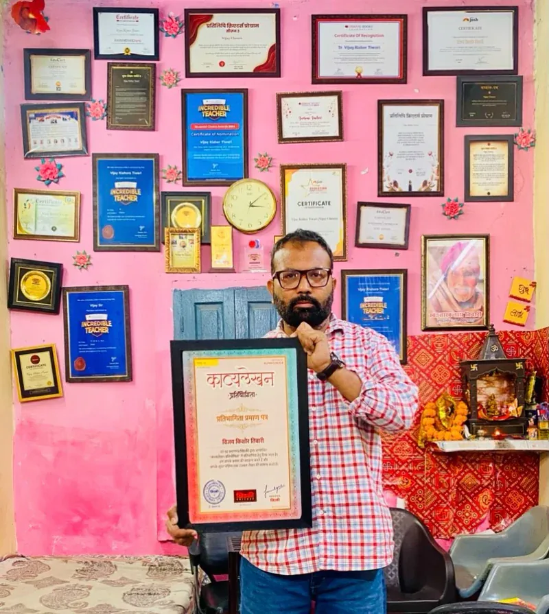 Vijay Kishor Tiwari holding a framed certificate in front of the wall of awards at Vijay Classes