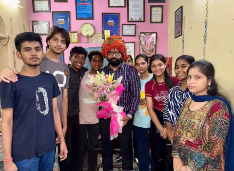 Vijay Kishor Tiwari in a turban holding a bouquet of flowers, with his students around him