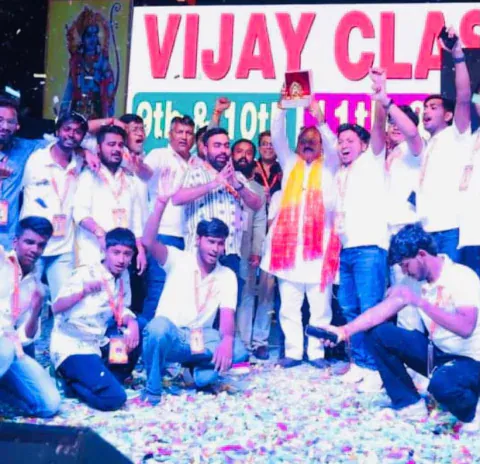Vijay Classes students and guests cheering on stage under a Vijay Classes banner, with confetti on the floor