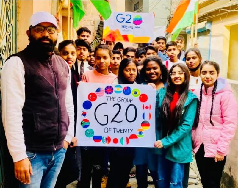 Vijay Kishor Tiwari with his students outside the centre, holding a hand-made G20 poster decorated with the flags of member countries