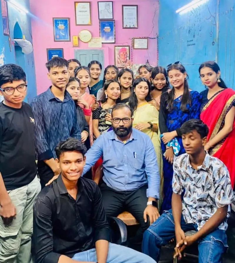 Vijay Kishor Tiwari seated among a large group of his students inside Vijay Classes, with awards and certificates on the wall behind them